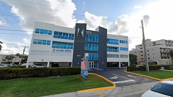 Edificio de cuatro plantas con letrero de New Life Plastic Surgery, ventanas azules, entrada para vehículos, acera y un automóvil