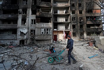 A local resident pushes a wheelbarrow in front of an apartment building destroyed during Ukraine-Russia conflict in the besieged southern port city of Mariupol, Ukraine March 30, 2022. REUTERS/Alexander Ermochenko