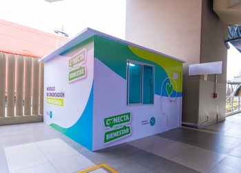 Módulo de orientación psicológica blanco, verde y azul con ventanas y textos 'Módulo de orientación psicológica' y 'Conecta con tu Bienestar' en una estación de metro