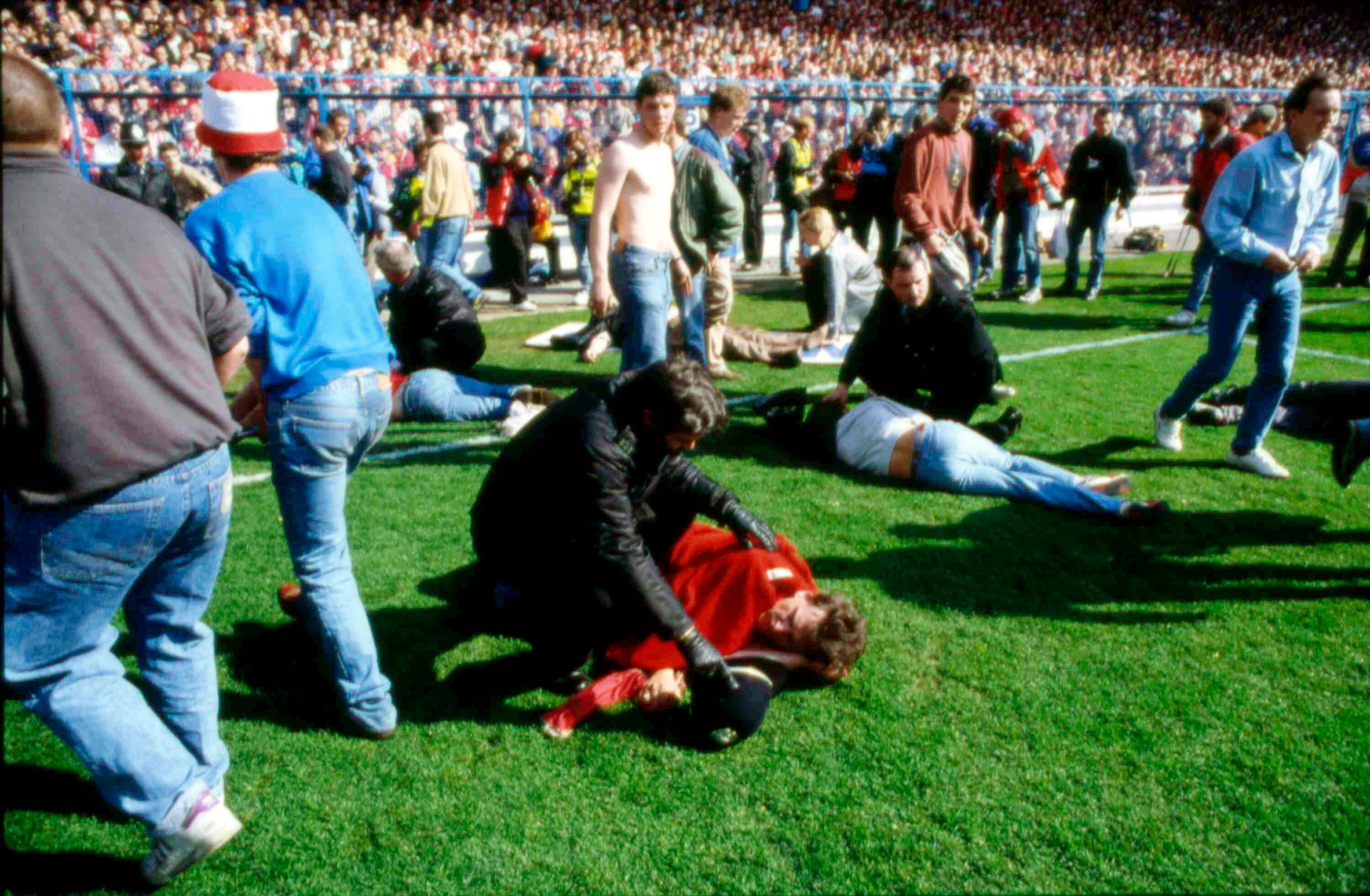 ARCHIVO - En foto del 15 de abril de 1989, seguidores y guardias de seguridad atienden a los aficionados tras el desastre en el Estadio de Hillsborough en Sheffield, Inglaterra. (AP Foto, Archivo)