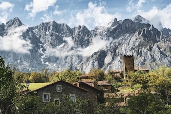 El paisaje lleno de montañas rocosas al fondo tiene en primer plano un pueblo de roca escondido entre vegetación verde.