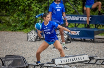 Una mujer vestida con un uniforme azul de Exatlón México, con el nombre Katia, sostiene una pelota azul preparándose para lanzarla en un circuito