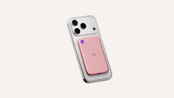Un teléfono inteligente gris con un pequeño dispositivo rectangular rosado adherido a la parte trasera sobre un fondo blanco