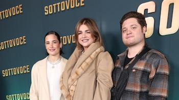 Toto Kirzner, con barba y camisa a cuadros, sonríe junto a dos mujeres con cabello castaño y ropa elegante frente a un fondo oscuro con texto dorado