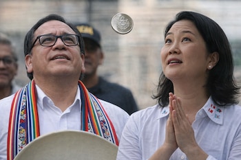 Roberto Sánchez y Keiko Fujimori, vestidos de blanco, miran hacia arriba una moneda suspendida en el aire, con otras personas de fondo.