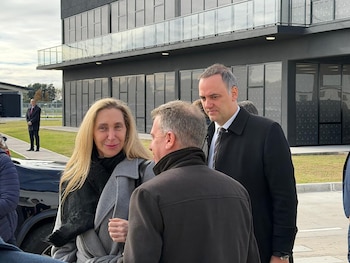 Manuel Adorni y Karina Milei conversan al aire libre frente a un edificio moderno de Mercedes Benz Camiones y Buses con un balcón de vidrio