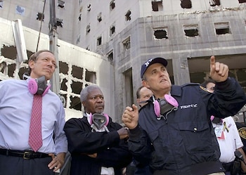 Rudy Giuliani, George Pataki y Kofi Annan, con respiradores colgando de sus cuellos, observan un edificio dañado con ventanas rotas en el sitio del 11S