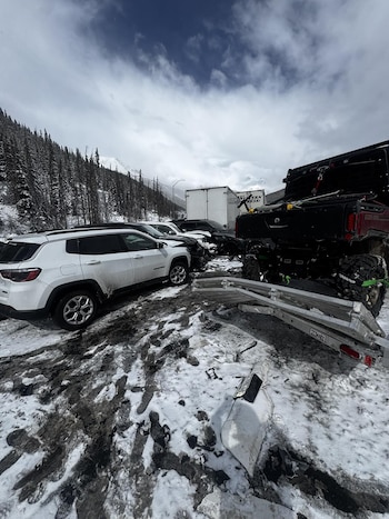 Varios coches, SUVs y un camión están involucrados en un accidente en una carretera cubierta de nieve y aguanieve, con montañas boscosas al fondo bajo un cielo nublado