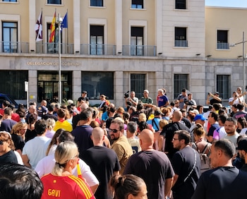 Una multitud de personas reunidas en la calle ante un edificio con el letrero Delegación del Gobierno y banderas en la fachada