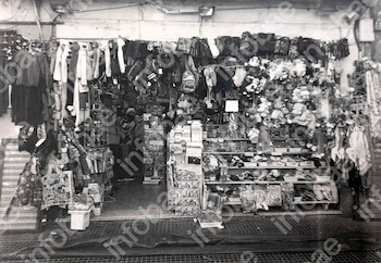 Puesto de mercado de pulgas B/N, lleno de ropa, mochilas, peluches y artículos variados exhibidos en estantes y colgados