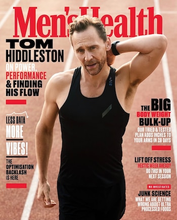Tom Hiddleston visto de frente con camiseta negra de tirantes y una mano tras la nuca en una pista de atletismo roja