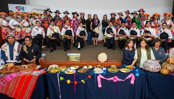 Un grupo de personas posa, algunas con vestimenta tradicional y sombreros, junto a una mesa con múltiples platos de comida y un lechón asado
