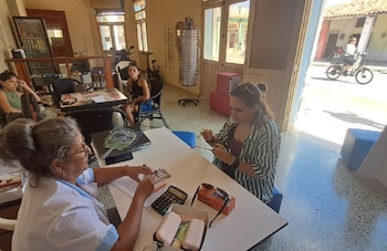 Interior de una óptica con exhibidores de anteojos en las paredes, un espejo octogonal, exhibidores giratorios y varias personas sentadas