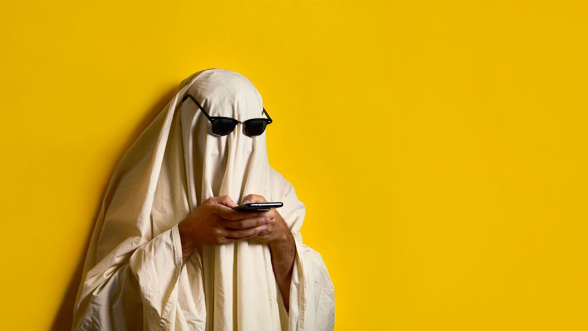 Una persona disfrazada de fantasma, mientras chatea (Canva)