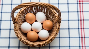 Una cesta de mimbre, siete huevos (cuatro blancos y tres marrones), y un mantel a cuadros azules y rojos