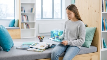 Una joven sentada en un banco de madera sostiene una tableta con un globo terráqueo digital, junto a libros abiertos y lápices.