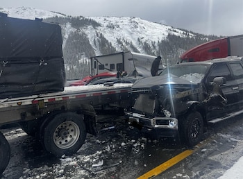 Accidente vial con un camión, una camioneta y otros vehículos dañados en una autopista con nieve. Montañas nevadas y árboles visibles al fondo