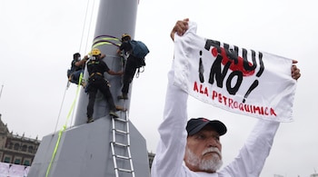 Un hombre sostiene un cartel con el texto Aquí no a la petroquímica mientras tres personas escalan una gran estructura metálica con arneses.