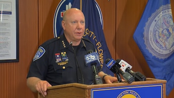 Hombre calvo con uniforme de policía de Rochester, Nueva York, habla ante micrófonos en un podio. Detrás hay dos banderas de la ciudad de Rochester