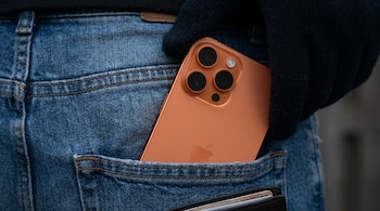 Primer plano de una mano enguantada de oscuro sacando un iPhone 17 Pro Max color cobre del bolsillo trasero de unos pantalones vaqueros azules.