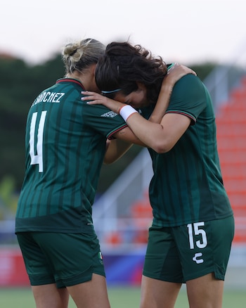 Dos jugadoras de fútbol femenino con uniforme verde oscuro, una con dorsal 11 y nombre Sánchez, abrazadas en un campo de juego