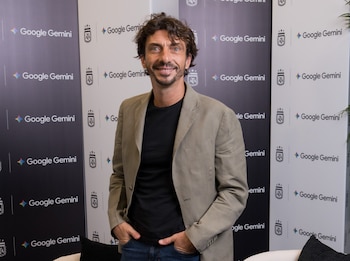 Ramiro Sánchez, un hombre de tez morena y cabello castaño rizado, sonríe a cámara vistiendo una camiseta negra y blazer beige, frente a un muro con logos de Google Gemini y AFA