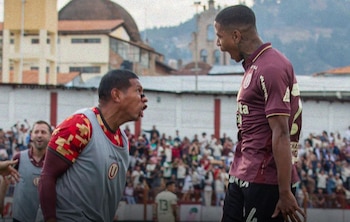 Dos integrantes del club Universitario vistiendo atuendo deportivo gritan de frente en un estadio de fútbol con público