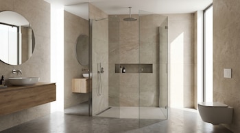 Baño moderno con azulejos claros, ducha con mamparas de vidrio sin marco, lavabo sobre mueble de madera, espejo redondo y un inodoro suspendido.