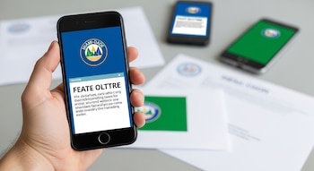 Mano sostiene smartphone con pantalla mostrando un logo falso de Miami-Dade y notificación de texto. Otros teléfonos y papeles oficiales desenfocados al fondo.