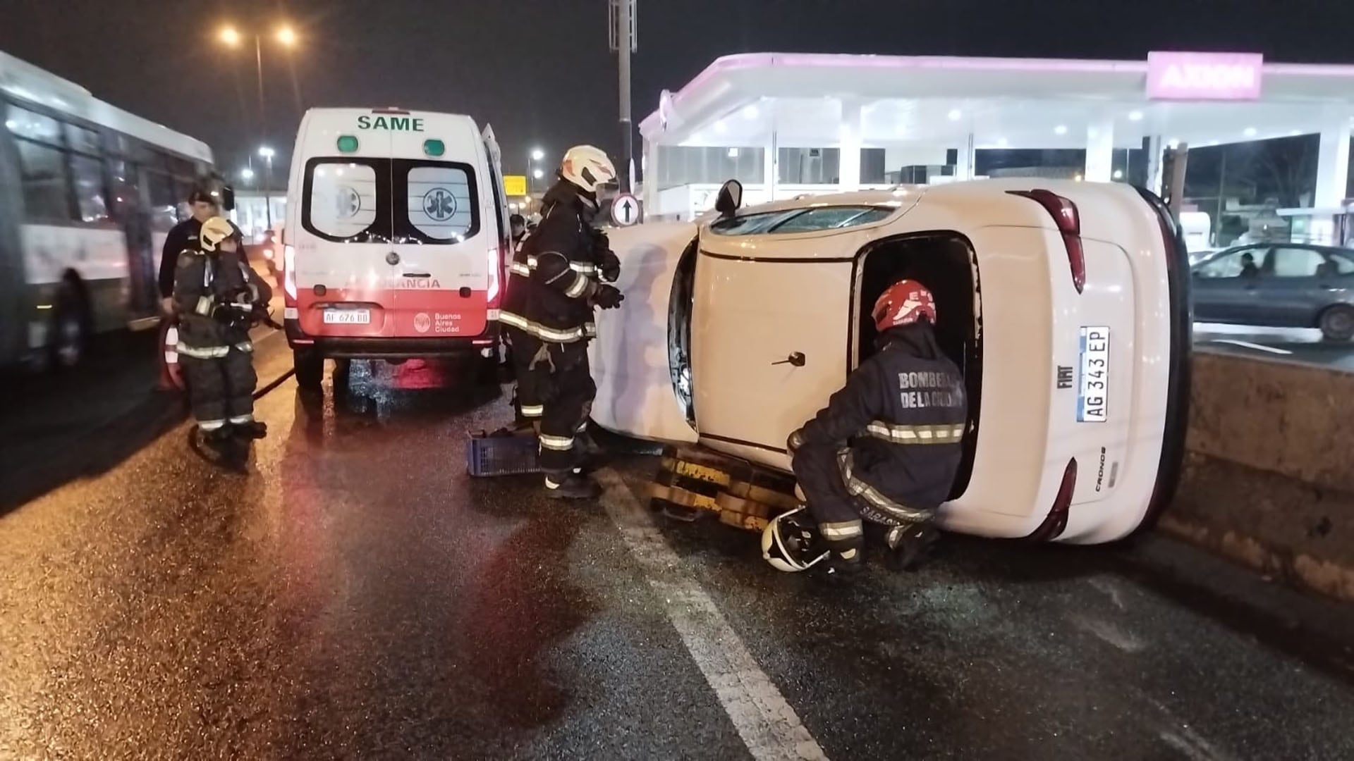Bomberos de la Ciudad y personal del SAME trabajan en el sitio de un choque con vuelco de un vehículo particular en la avenida General Paz durante la noche.