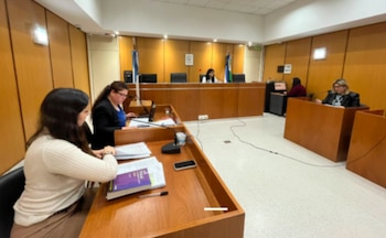 Interior de sala de audiencias con varias mujeres sentadas en escritorios de madera, documentos apilados, teléfonos móviles y micrófonos sobre las mesas