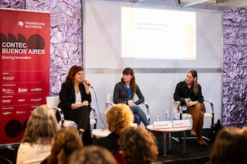 Tres mujeres en un panel de discusión, una de ellas habla por un micrófono. Detrás, un banner rojo de CONTEC Buenos Aires y una pantalla proyecta un título