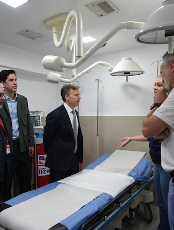 Varias personas conversan junto a una camilla en un área médica provista de lámparas quirúrgicas articuladas y equipos de asistencia