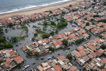 Vista aérea de un distrito costero con casas de techos de teja, calles inundadas con vehículos sumergidos, áreas verdes anegadas y el mar adyacente.