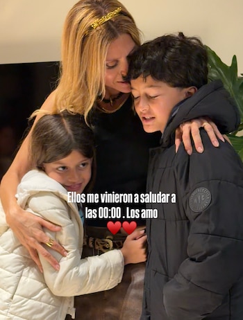 Una mujer con tiara dorada abraza a una niña con abrigo blanco y a un niño con abrigo negro, con texto sobreimpreso en el centro