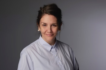 Retrato de una mujer de mediana edad con cabello oscuro recogido, usando una camisa azul claro y pendientes de perlas, sonriendo ligeramente