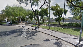 Calle empedrada con la inscripción Obispo San Alberto, una motocicleta en la acera, árboles, farolas y un vehículo blanco estacionado