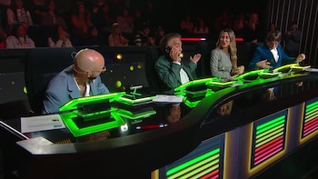 Cuatro personas sentadas en una mesa con luces fluorescentes verdes en un estudio de televisión mientras una de ellas habla por teléfono