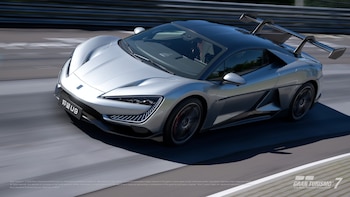 Un coche deportivo Yangwang U9 plateado y negro con un gran alerón trasero se mueve rápidamente sobre una pista de carreras con barreras al fondo