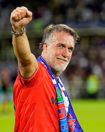 Gabriel Batistuta sonríe y levanta el puño derecho mientras viste una camiseta roja y una bufanda deportiva sobre los hombros