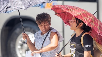 Dos mujeres caminan en la calle bajo el sol mientras se cubren la cabeza con sombrillas