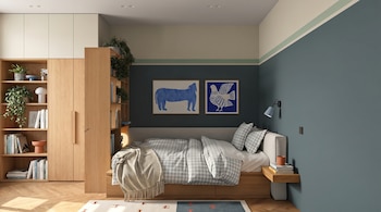 Vista frontal de un dormitorio moderno con paredes bicolor, cama con edredón a cuadros grises, estantería de madera y dos cuadros azules sobre la cama.