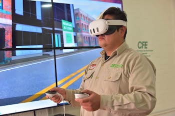 Hombre usando gafas y controladores de realidad virtual. Una pantalla grande detrás muestra una calle virtual y edificios. El logo de CFE es visible en la pared derecha
