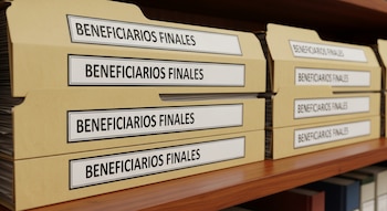 Varias carpetas de cartulina marrón claro con etiquetas blancas que dicen "BENEFICIARIOS FINALES" se apilan en dos hileras sobre un estante de madera.