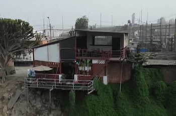 Un inmueble de dos niveles con estructura de madera y terraza se encuentra construido al borde de un terreno con erosión y vegetación