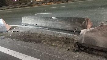 Barreras de concreto gris dañadas en el borde de una carretera asfaltada oscura con líneas blancas, tierra y escombros junto a un guardarraíl metálico