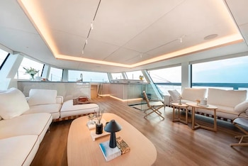 Salón con sofás blancos, mesas de centro de madera, suelo de parqué y ventanales panorámicos con vista al mar desde una embarcación