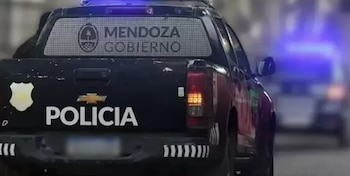 Vista trasera de camioneta policial oscura. Placa con escudo y texto Mendoza Gobierno. Texto Policía en la compuerta. Emblema Chevrolet. Luces azules