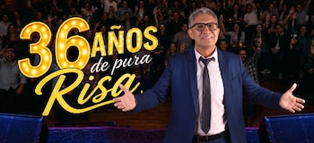 Fernando Armas viste traje azul frente al cartel luminoso con la frase 36 años de pura risa y un público de fondo