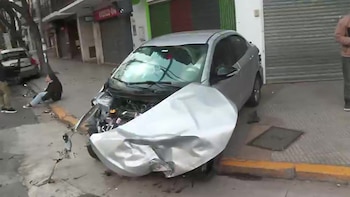 Un automóvil gris chocado sobre la acera con la parte frontal destruida frente a un local comercial cerrado